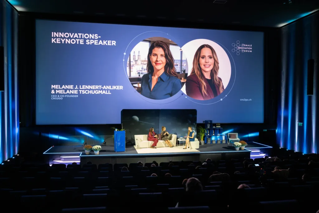 Moderatorin Sunnie Groeneveld im Gespräch mit Melanie J. Lennert-Anliker und Melanie Tschugmall von CRO2go auf der Bühne des Female Innovation Forum 2026 vor dem Publikum im Kinosaal.