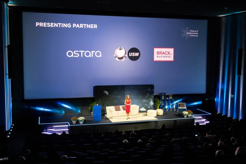Moderatorin Sunnie Groeneveld auf der Bühne des Female Innovation Forum 2026 vor einer Leinwand mit den Logos der Presenting Partner astara, USM und Brack.Business.