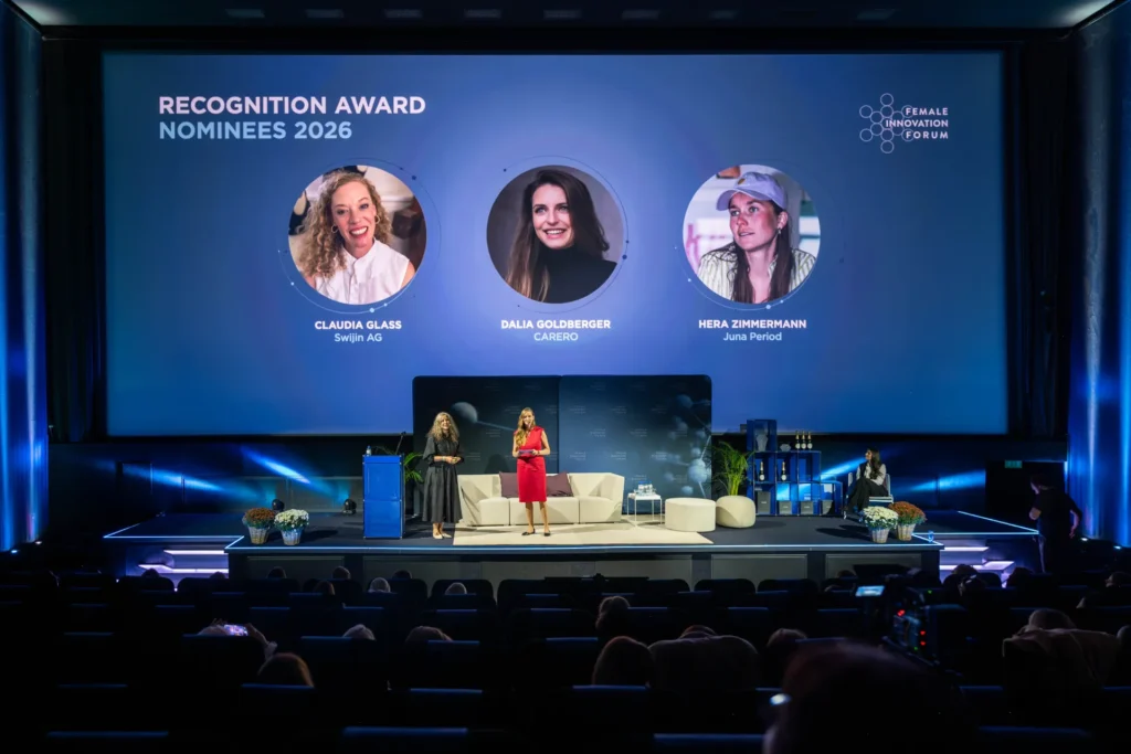 Sandra-Stella Triebl und Sunnie Groeneveld auf der Bühne des Female Innovation Forum 2026. Auf der Leinwand sind die drei Nominierten Claudia Glass, Dalia Goldberger und Hera Zimmermann zu sehen.